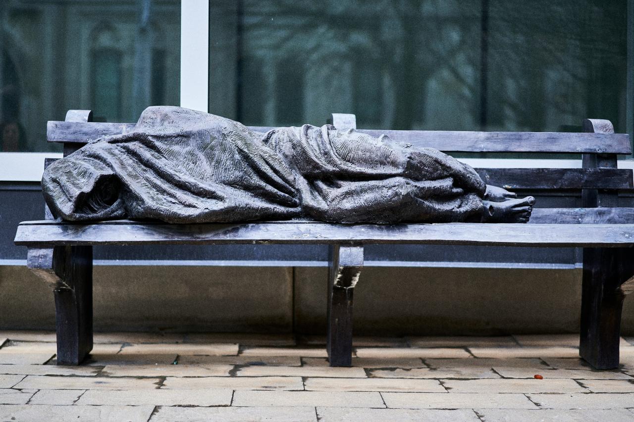 Statue of a person depicted to be experiencing homelessness cast on a bench in Toronto. Photo courtesy of Ashwini Chaudhary on Unsplash