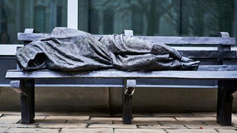 Statue of a person depicted to be experiencing homelessness cast on a bench in Toronto. Photo courtesy of Ashwini Chaudhary on Unsplash